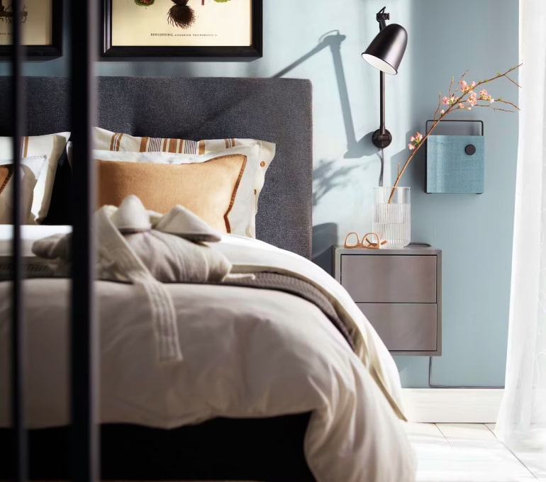Sovrum med grå sänggavel, beige sängkläder och blå vägg
